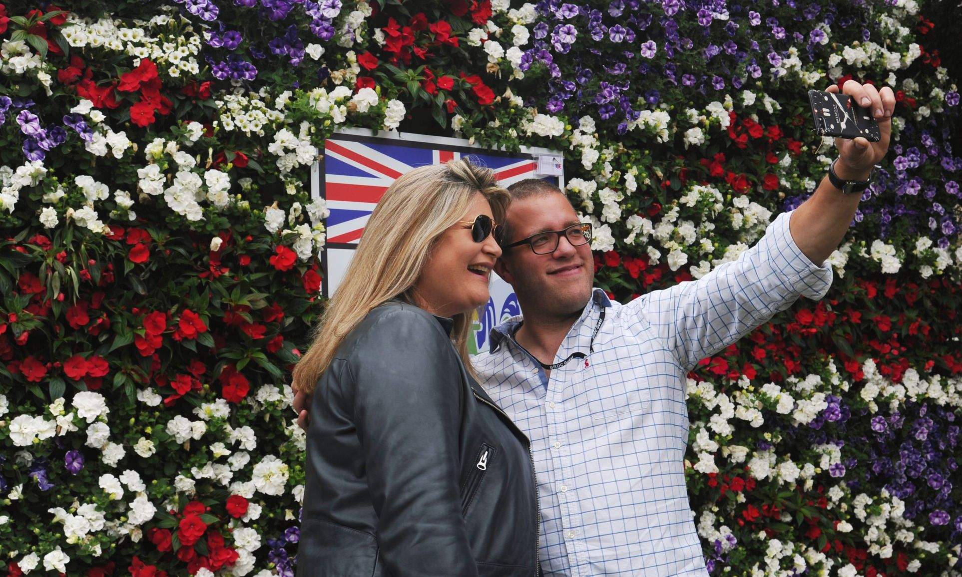 This is an image of a couple taking a selfie in front of a Union Jack designed Wonderwall living wall at Silverstone.